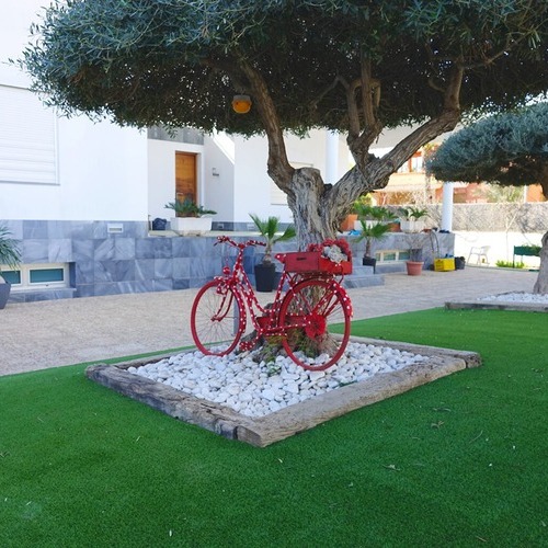 artificial turf surrounding a red bicycle sitting in front of a tree in a lawn outdoors